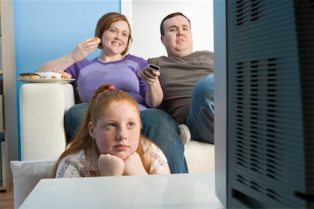 sitting in a sofa with snacks and tv remote - Overweight family watching television on sofa Stock Photo - Premium Royalty-Free, Code: 693-06016367