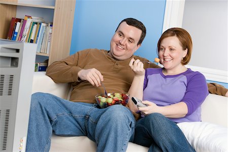 Overweight couple eating fruit on sofa Stock Photo - Premium Royalty-Free, Code: 693-06016372