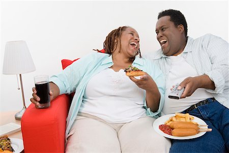 Mid-adult overweight couple sitting on sofa with meal and watching television Stock Photo - Premium Royalty-Free, Code: 693-06016425