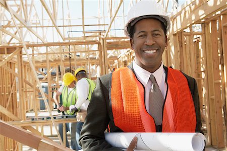 Smiling Surveyor in hard hat with building plans on Construction Site Foto de stock - Sin royalties Premium, Código: 693-06016698