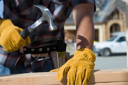 Construction worker hammering nail to wooden plank on construction site Stock Photo - Premium Royalty-Free, Code: 693-06016885