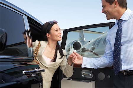 Businessman helping Woman Get Out of Car parked near private jet, side view Stock Photo - Premium Royalty-Free, Code: 693-06016939