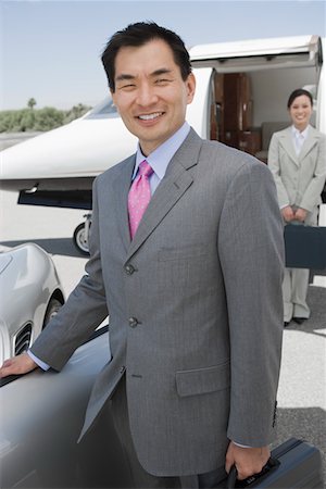 Portrait of mid-adult businessman standing in front of convertible, mid-adult businesswoman in background. Foto de stock - Royalty Free Premium, Número: 693-06016957