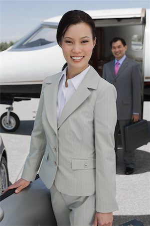 Portrait of mid-adult businesswoman standing in front of convertible, mid-adult businessman in background. Stock Photo - Premium Royalty-Free, Code: 693-06016958