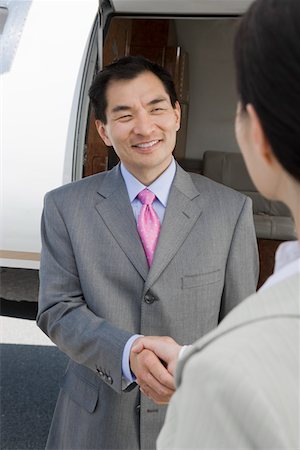 Mid-adult Asian businessman shaking hands with mid-adult businesswoman in front of private plane. Stock Photo - Premium Royalty-Free, Code: 693-06016960