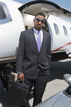 African-American businessman standing in front of private airplane and car. Stock Photo - Premium Royalty-Free, Code: 693-06016972