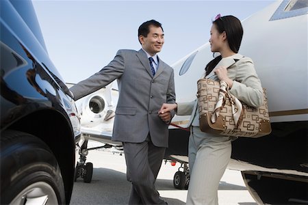 Mid-adult Asian businesswoman and businessman flirting outside of car and airplane. Stock Photo - Premium Royalty-Free, Code: 693-06016991