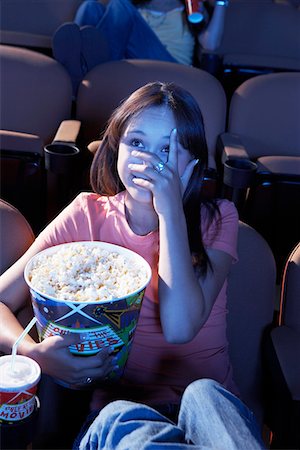 people scared movie theatre - Young woman holding Popcorn, covering face with hand, watching movie in Theatre Stock Photo - Premium Royalty-Free, Code: 693-06017215