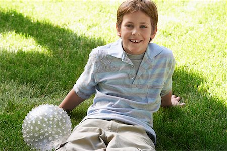 Boy with ball sitting on park lawn, portrait Stock Photo - Premium Royalty-Free, Code: 693-06018460