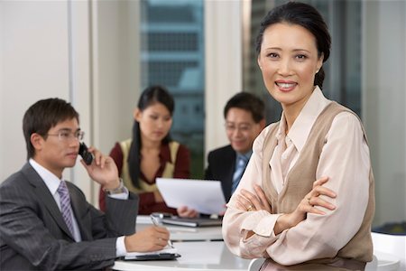 simsearch:693-06019591,k - Business woman sitting at conference table with colleagues in background, portrait Stock Photo - Premium Royalty-Free, Code: 693-06018475