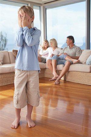 Boy standing, Hiding Face from Family in Background Stock Photo - Premium Royalty-Free, Code: 693-06018581