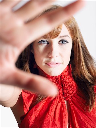 Woman in red top  in studio, view past woman's hand Stock Photo - Premium Royalty-Free, Code: 693-06018610