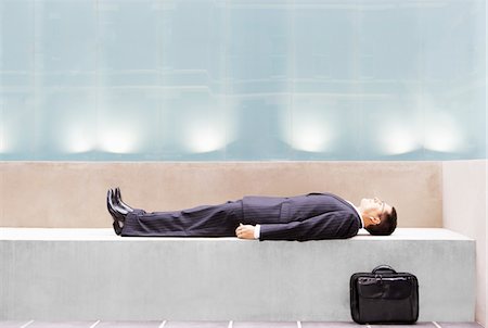 Businessman lying on concrete bench, side view Stock Photo - Premium Royalty-Free, Code: 693-06018777
