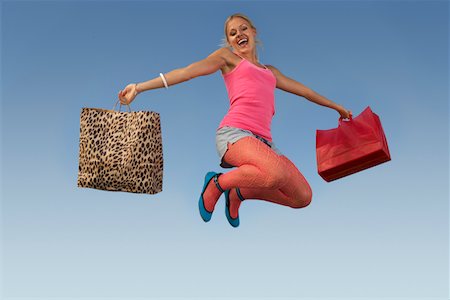 Portrait of young woman jumping with shopping bags in park Stock Photo - Premium Royalty-Free, Code: 693-06019416