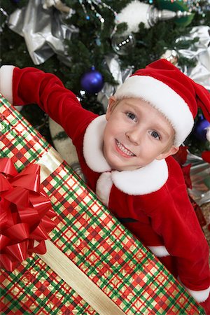 Boy (5-6) in Santa costume holding present by Christmas tree Stock Photo - Premium Royalty-Free, Code: 693-06019536