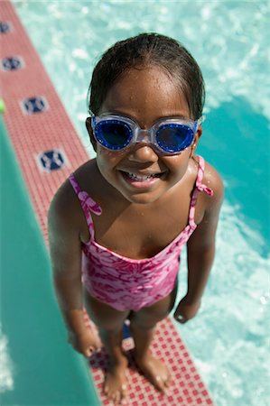 Girl (5-6) Wearing swim Goggles standing on Edge of Swimming Pool, elevated view portrait. Stock Photo - Premium Royalty-Free, Code: 693-06013556