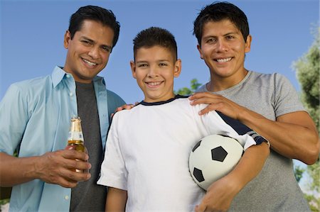 Boy (13-15) holding soccer ball, standing with two brothers, one brother holding beer bottle, front view. Stock Photo - Premium Royalty-Free, Code: 693-06013612