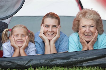 Mother, daughter and grand-daughter lean on elbows, smiling from tent Stock Photo - Premium Royalty-Free, Code: 693-06021498