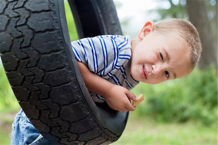 person winking - Portrait of a young boy winking while swinging on tire Stock Photo - Premium Royalty-Free, Code: 693-06120672