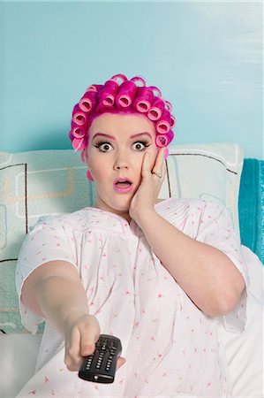 simsearch:693-06120757,k - Portrait of shocked woman holding remote with hair curlers sitting on bed Stock Photo - Premium Royalty-Free, Code: 693-06120724