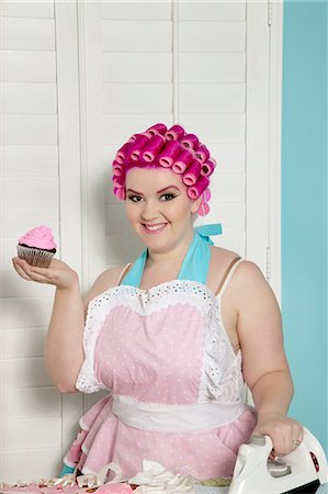 fat woman cleaning house - Portrait of happy young woman holding cupcake while ironing Stock Photo - Premium Royalty-Free, Code: 693-06120742
