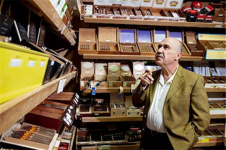 Small tobacco store owner looking at cigar boxes on display in shop Stock Photo - Premium Royalty-Free, Code: 693-06120801