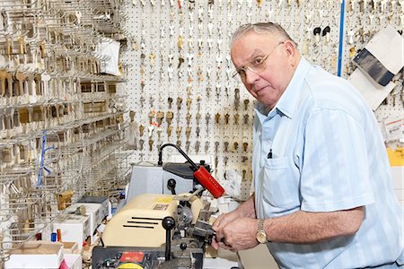 Senior locksmith looking away while making key in store Foto de stock - Royalty Free Premium, Número: 693-06120842