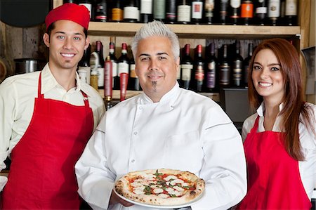 Portrait of a happy chef holding pizza with wait staff Stock Photo - Premium Royalty-Free, Code: 693-06120858