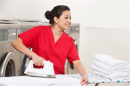 simsearch:693-06379358,k - Happy young female employee ironing while looking away in Laundromat Foto de stock - Sin royalties Premium, Código: 693-06120892