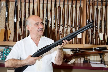 Mature gun store owner looking at weapon in shop Foto de stock - Sin royalties Premium, Código: 693-06120917