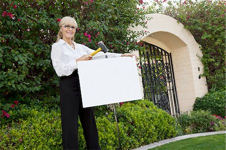 Portrait of a happy senior female agent hammering sign board in lawn Fotografie stock - Premium Royalty-Free, Codice: 693-06120911