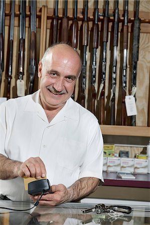 shopkeeper man - Portrait of a mature merchant with credit card reader in gun shop Stock Photo - Premium Royalty-Free, Code: 693-06120927