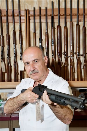 Mature gun merchant with rifle looking away Fotografie stock - Premium Royalty-Free, Codice: 693-06120920