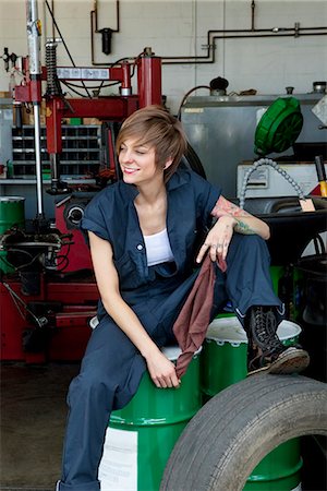 female mechanic - Happy young female mechanic sitting on oil drum in automobile repair shop Foto de stock - Sin royalties Premium, Código: 693-06120972