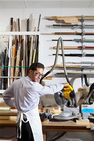 Portrait of a young man looking back while using circular saw in workshop Stock Photo - Premium Royalty-Free, Code: 693-06121006