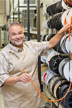 Portrait of a happy mature store clerk with electrical wire spool in hardware shop Stock Photo - Premium Royalty-Free, Code: 693-06121066