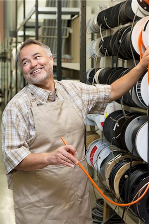 Happy mature salesperson standing by electrical wire spool while looking away in hardware store Stock Photo - Premium Royalty-Free, Code: 693-06121067