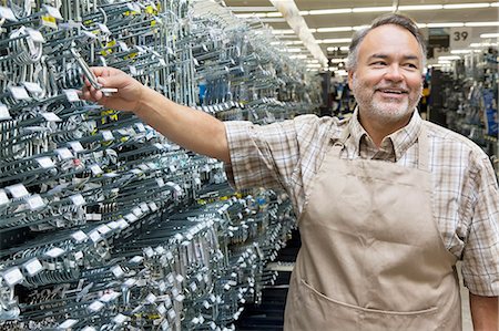 Happy mature salesperson holding metallic equipment while looking away in hardware store Stock Photo - Premium Royalty-Free, Code: 693-06121063