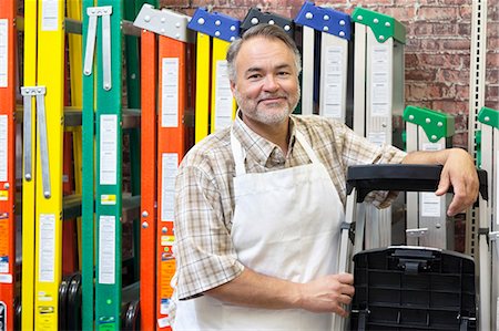 portrait of employees - Portrait of happy mature store clerk standing by multicolored ladders in hardware shop Stock Photo - Premium Royalty-Free, Code: 693-06121074