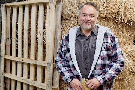 Portrait of happy mature male standing in front of hay stack Foto de stock - Royalty Free Premium, Número: 693-06121147