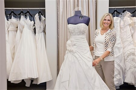 Portrait of a happy senior female adjusting wedding dress on mannequin in bridal store Stock Photo - Premium Royalty-Free, Code: 693-06121242