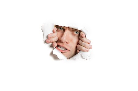 Portrait of a aggressive mid adult man peeking from ripped white paper hole Foto de stock - Sin royalties Premium, Código: 693-06121336