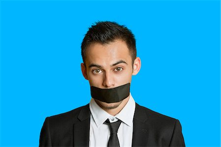 quiet - Portrait of a young businessman with adhesive tape on mouth over colored background Stock Photo - Premium Royalty-Free, Code: 693-06121342