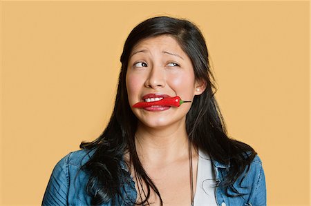 simsearch:693-06121348,k - Young woman with red chili pepper in mouth over colored background Stock Photo - Premium Royalty-Free, Code: 693-06121365