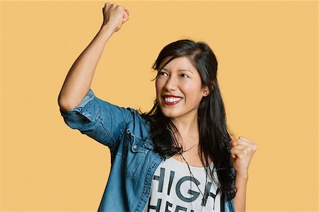 Excited young woman with raised fist while looking away over colored background Foto de stock - Sin royalties Premium, Código: 693-06121362