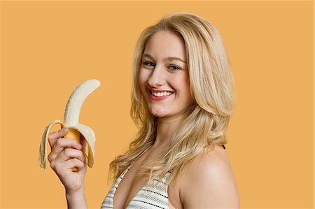 Portrait of a young woman eating banana over colored background Foto de stock - Royalty Free Premium, Número: 693-06121373