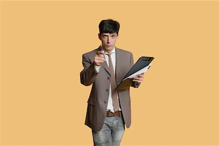 Portrait of a young businessman pointing while holding clipboard over colored background Stock Photo - Premium Royalty-Free, Code: 693-06121382