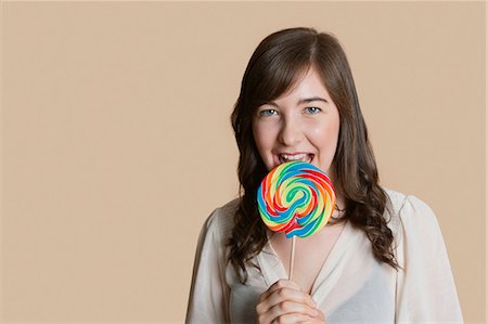 Portrait of a beautiful young woman with lollipop over colored background Stock Photo - Premium Royalty-Free, Code: 693-06121416