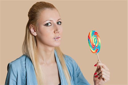 Portrait of a blond woman with sprinkled lips holding lollipop over colored background Stock Photo - Premium Royalty-Free, Code: 693-06121413