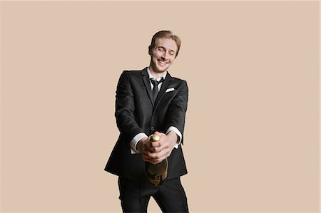 people celebrating new years eve - Portrait of a young businessman uncorking champagne over colored background Stock Photo - Premium Royalty-Free, Code: 693-06121422